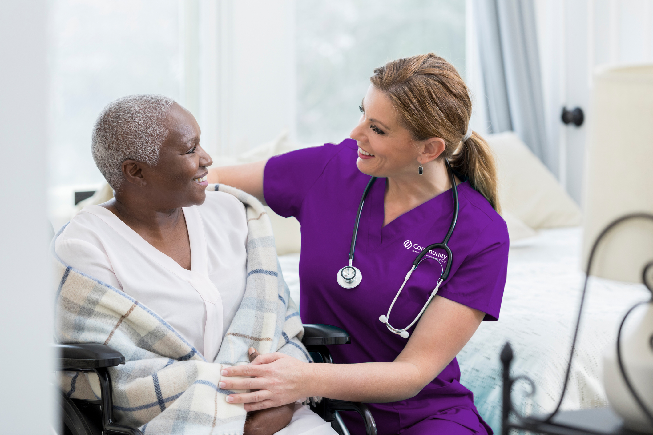 Nurse in Scrubs Comforting Elderly Woman in Blanket in Room Setting darker purple
